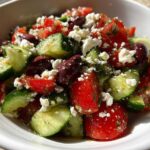 A vibrant close-up of Mediterranean Cucumber Tomato Salad featuring chunks of cucumber, tomato, Kalamata olives, and crumbled feta cheese.