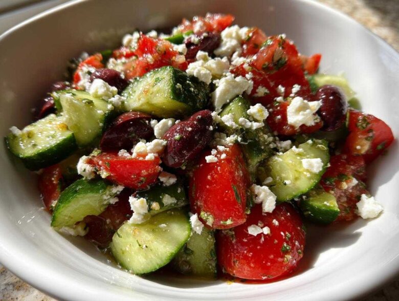 A vibrant close-up of Mediterranean Cucumber Tomato Salad featuring chunks of cucumber, tomato, Kalamata olives, and crumbled feta cheese.