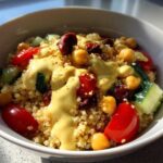 Close-up of a Mediterranean Quinoa Bowl topped with creamy lemon tahini sauce, chickpeas, tomatoes, and cucumber.