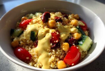 Close-up of a Mediterranean Quinoa Bowl topped with creamy lemon tahini sauce, chickpeas, tomatoes, and cucumber.
