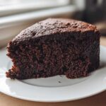 Close-up of a rich, dark slice of Gluten-Free Chocolate Cake on a white plate.