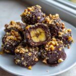 A stack of No-Bake Chocolate Covered Banana Bites, showing a cross-section revealing banana inside dark chocolate coating and chopped peanuts.