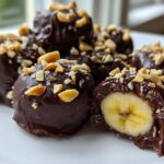 Close-up of No-Bake Chocolate Covered Banana Bites, showing a cross-section of banana inside chocolate coating and topped with chopped peanuts.