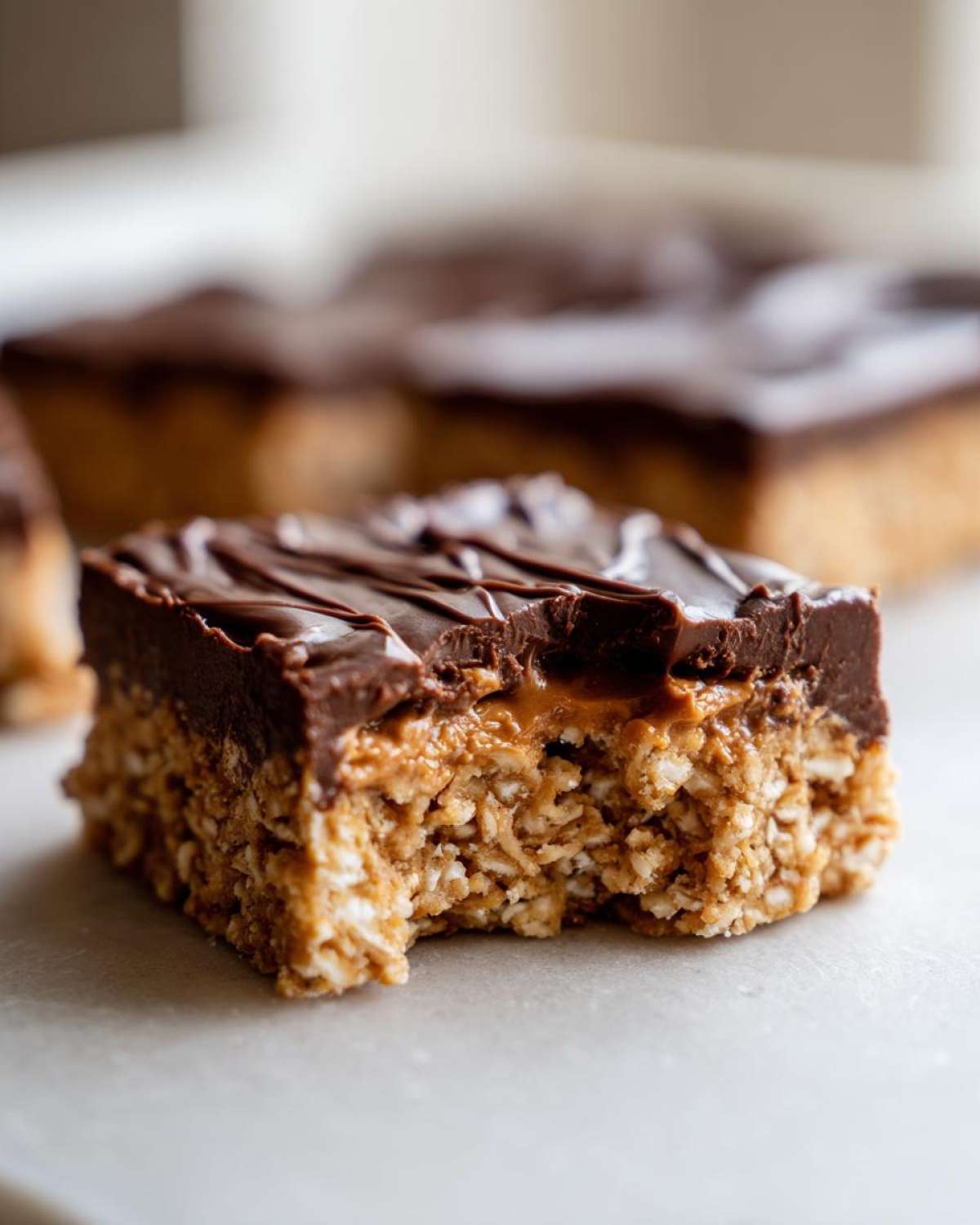 A close-up of a No-Bake Chocolate Peanut Butter Oat Bar with a bite taken out, showing the oat base and chocolate topping.
