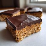 A close-up of a square No-Bake Chocolate Peanut Butter Oat Bars piece showing the oat base and thick chocolate topping.