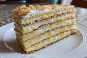 A tall slice of No-Bake Lemon Icebox Cake showing layers of graham crackers, lemon filling, and whipped cream.
