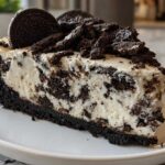 A close-up of a rich slice of No-Bake Oreo Cheesecake featuring a thick Oreo crust and creamy filling studded with cookie pieces.