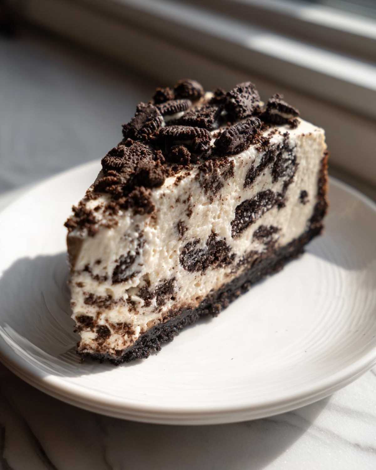 A perfect slice of No-Bake Oreo Cheesecake with a dark Oreo crust and creamy filling mixed with cookie pieces.