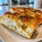 Close-up of a thick, airy slice of No-Knead Skillet Focaccia with Rosemary, showing olive oil pooling in the holes.
