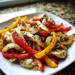 A white plate filled with seasoned slices of chicken, red and yellow bell peppers, and onions from One-Pan Chicken Fajitas with Peppers and Onions.