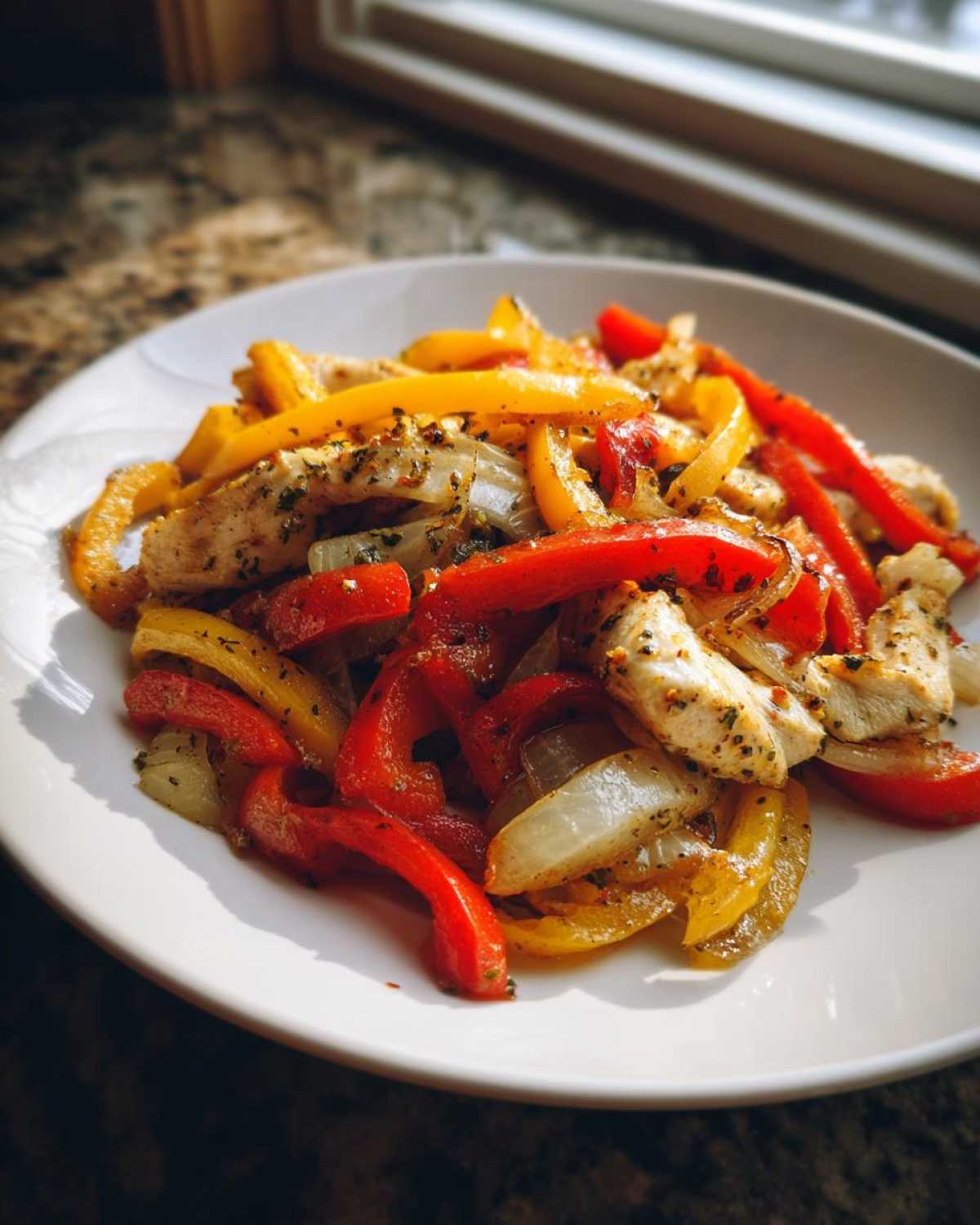 A close-up of seasoned chicken strips mixed with sautéed red and yellow bell peppers and onions, ready to eat, from the One-Pan Chicken Fajitas recipe.