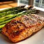 A perfectly cooked fillet of One-Pan Lemon Garlic Salmon served next to bright green roasted asparagus on a white plate.