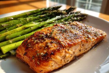 A perfectly cooked fillet of One-Pan Lemon Garlic Salmon served next to bright green roasted asparagus on a white plate.