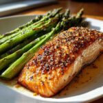 A perfectly cooked fillet of One-Pan Lemon Garlic Salmon topped with seasoning, served next to bright green roasted asparagus.