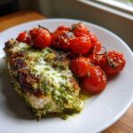 A serving of One-Pan Pesto Chicken with Tomatoes, featuring a pesto-crusted chicken breast topped with melted cheese and roasted cherry tomatoes.