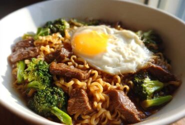 A close-up of One-Pot Beef and Broccoli Ramen Noodles topped with a sunny-side-up egg in a white bowl.