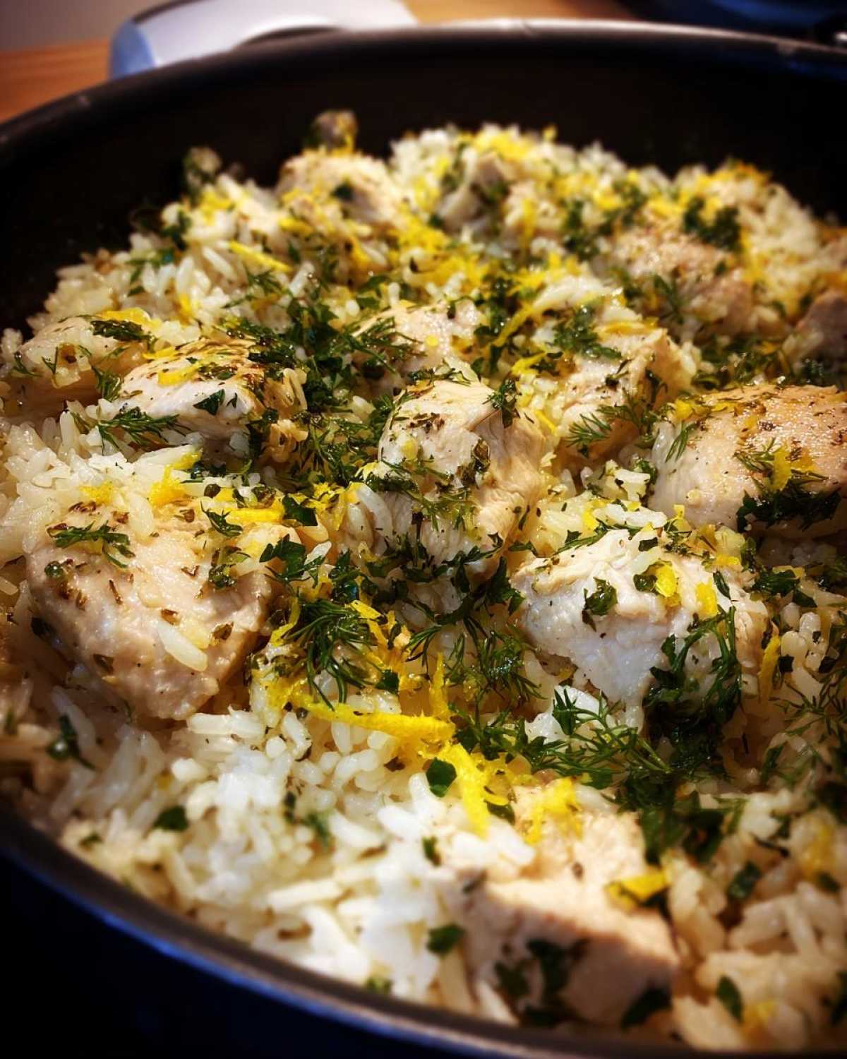 Close-up of tender chicken pieces mixed with fluffy white rice, topped generously with fresh herbs and bright yellow lemon zest for One-Pot Chicken and Rice with Lemon and Herbs.