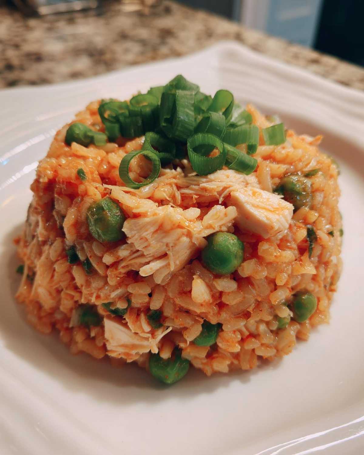 A mound of flavorful One-Pot Chicken Jambalaya mixed with chicken and peas, topped with fresh green onions.