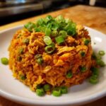 A molded serving of vibrant orange One-Pot Chicken Jambalaya mixed with peas and topped generously with fresh sliced green onions.
