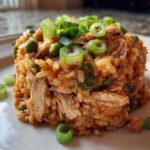 A molded serving of flavorful One-Pot Chicken Jambalaya featuring shredded chicken, rice, and peas, topped with fresh green onions.