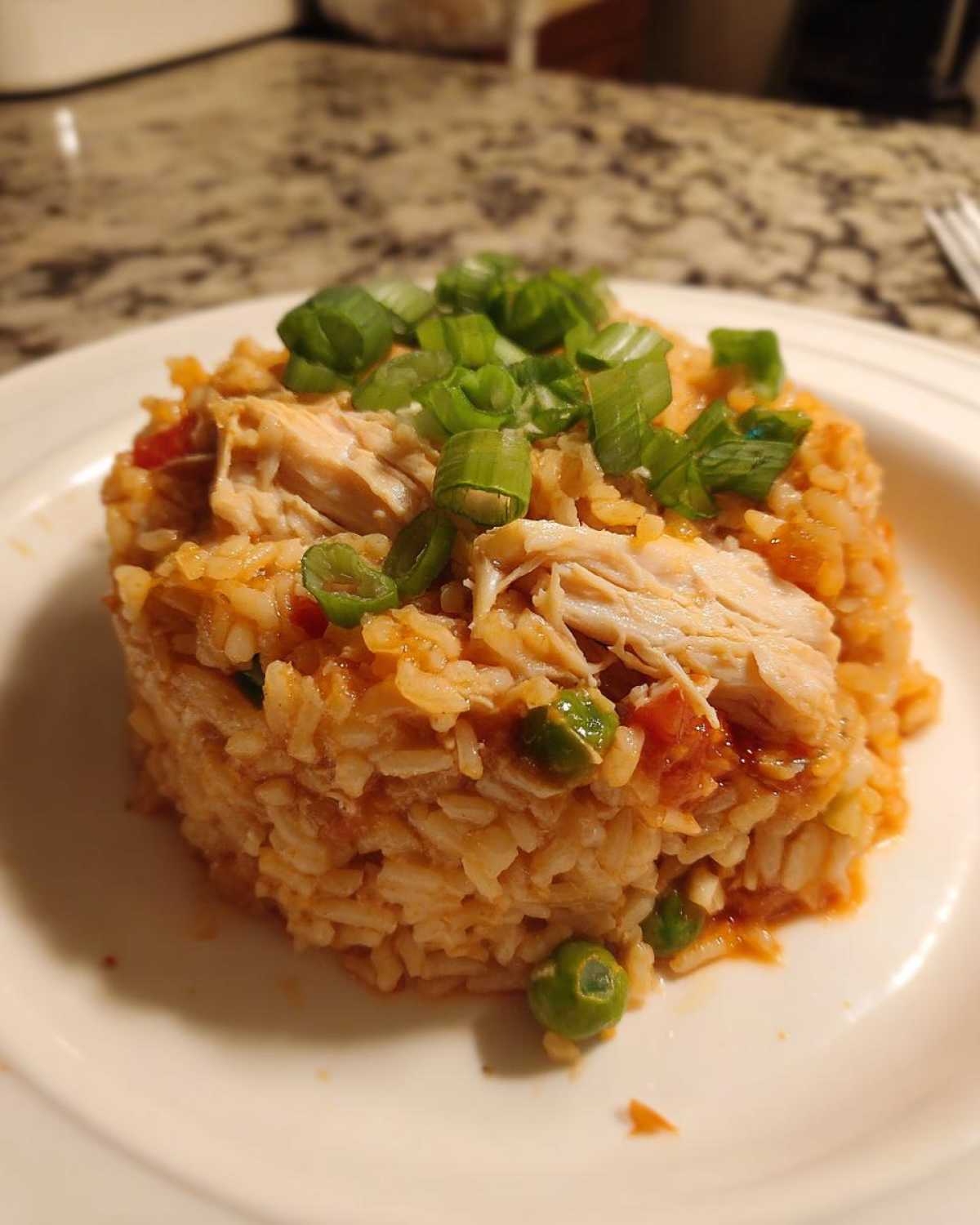 A molded serving of One-Pot Chicken Jambalaya featuring shredded chicken, rice, and peas, topped with chopped green onions.