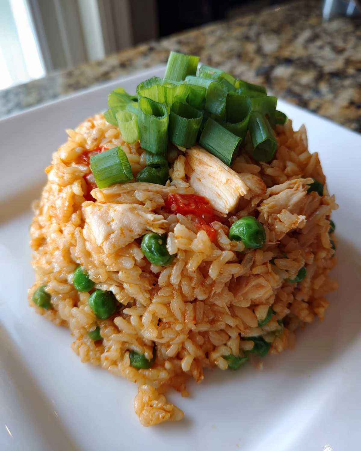 A molded serving of One-Pot Chicken Jambalaya featuring rice, chicken pieces, peas, and topped with fresh chopped green onions.