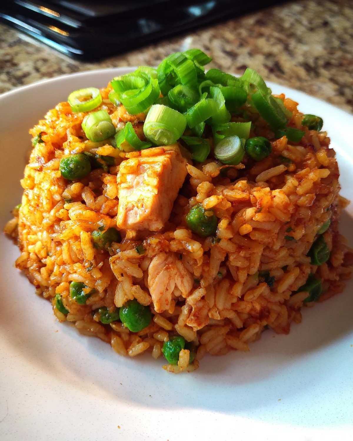 A mound of flavorful One-Pot Chicken Jambalaya mixed with peas and topped with fresh green onions.