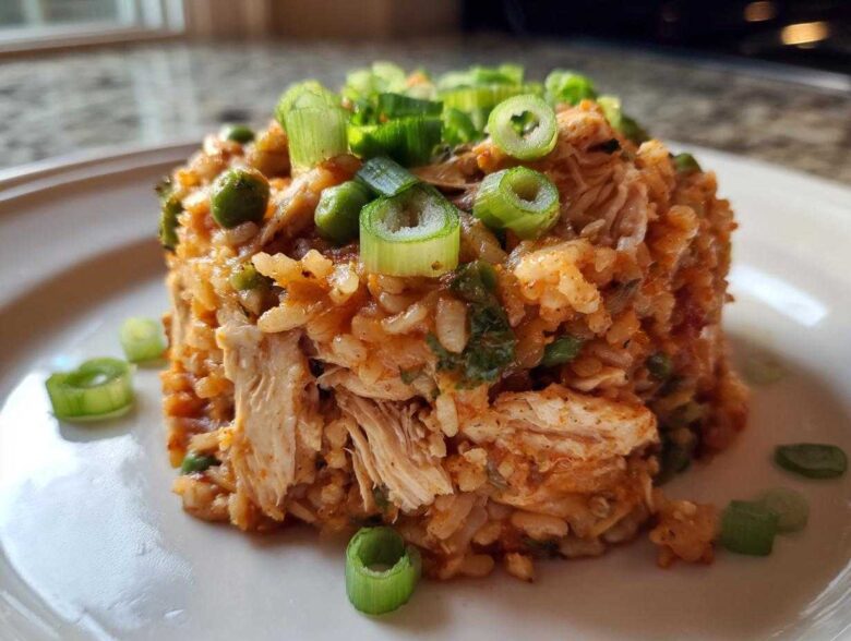 A molded serving of flavorful One-Pot Chicken Jambalaya featuring shredded chicken, rice, and peas, topped with fresh green onions.