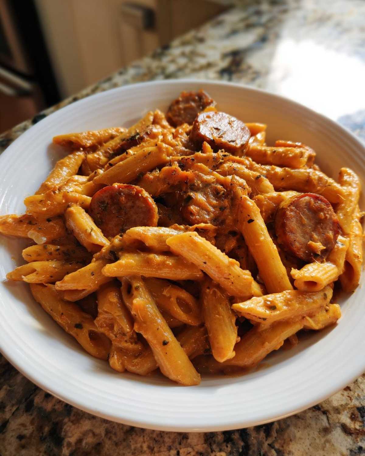 A white bowl filled with One-Pot Creamy Cajun Sausage Pasta featuring penne noodles and sliced sausage.