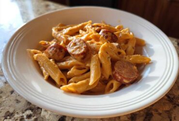 Close-up of a white bowl filled with One-Pot Creamy Cajun Sausage Pasta featuring penne and sliced sausage.