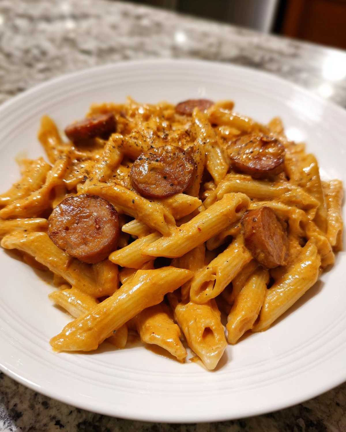 A close-up of a white bowl filled with One-Pot Creamy Cajun Sausage Pasta topped with sliced sausage.