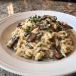 A close-up of One-Pot Creamy Mushroom Orzo garnished with fresh parsley on a white plate.