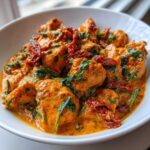 A close-up of chunks of chicken coated in a rich, orange-hued sauce with spinach and sun-dried tomatoes: One-Pot Creamy Sun-Dried Tomato Chicken.