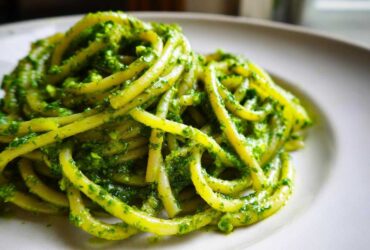 Close-up of thick pasta noodles coated generously in bright green Vegan Basil Pesto on a white plate.