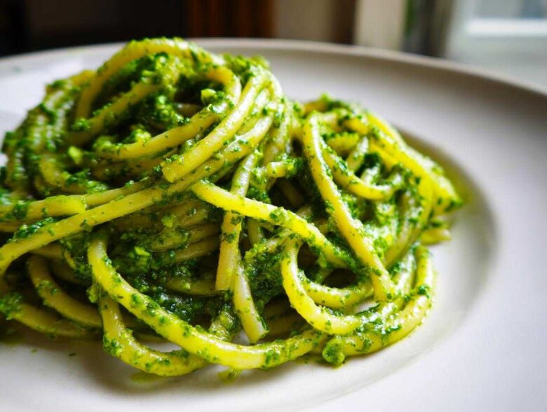 Close-up of thick pasta noodles coated generously in bright green Vegan Basil Pesto on a white plate.