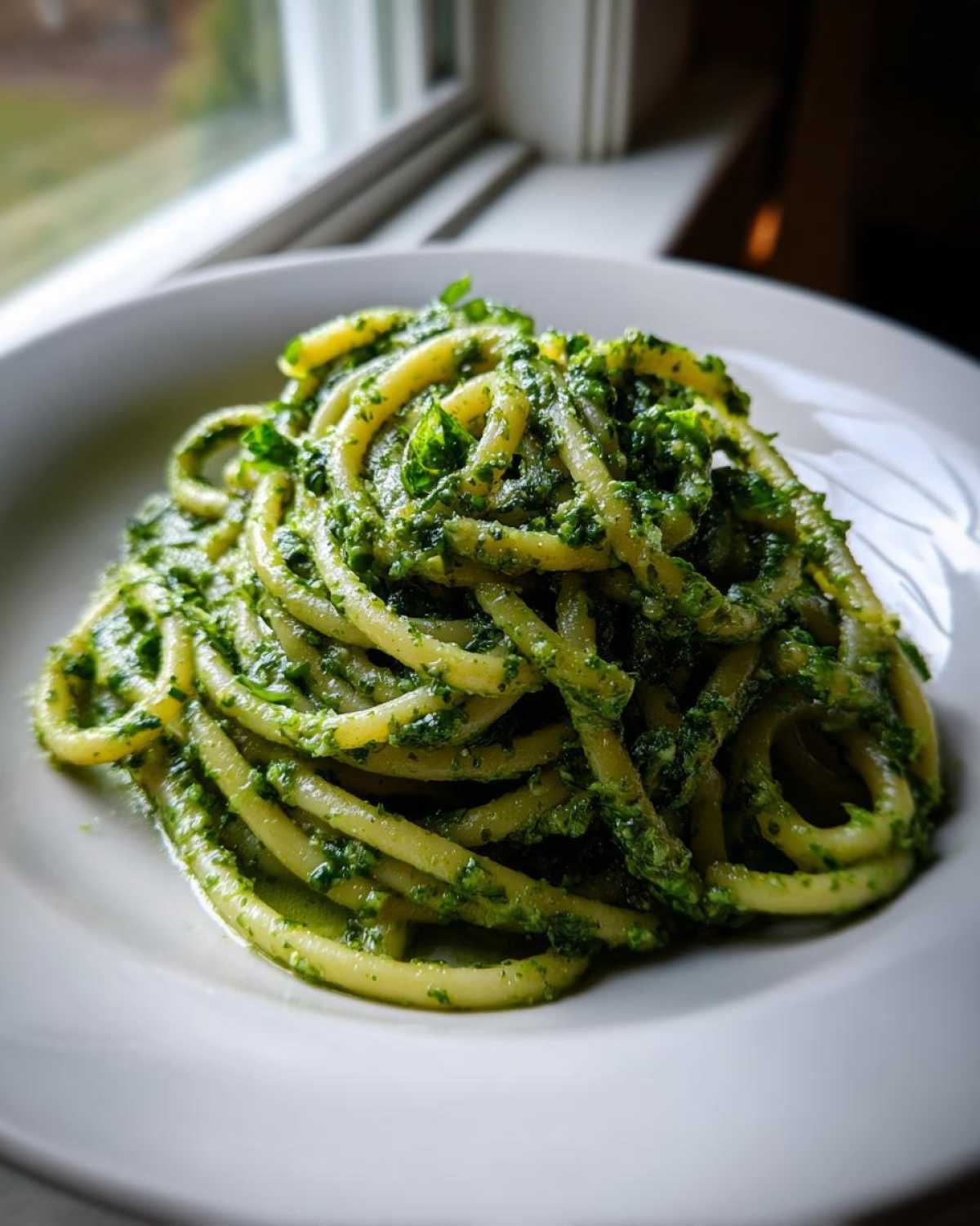 A close-up of thick pasta tossed generously with vibrant green Vegan Basil Pesto sauce on a white plate.