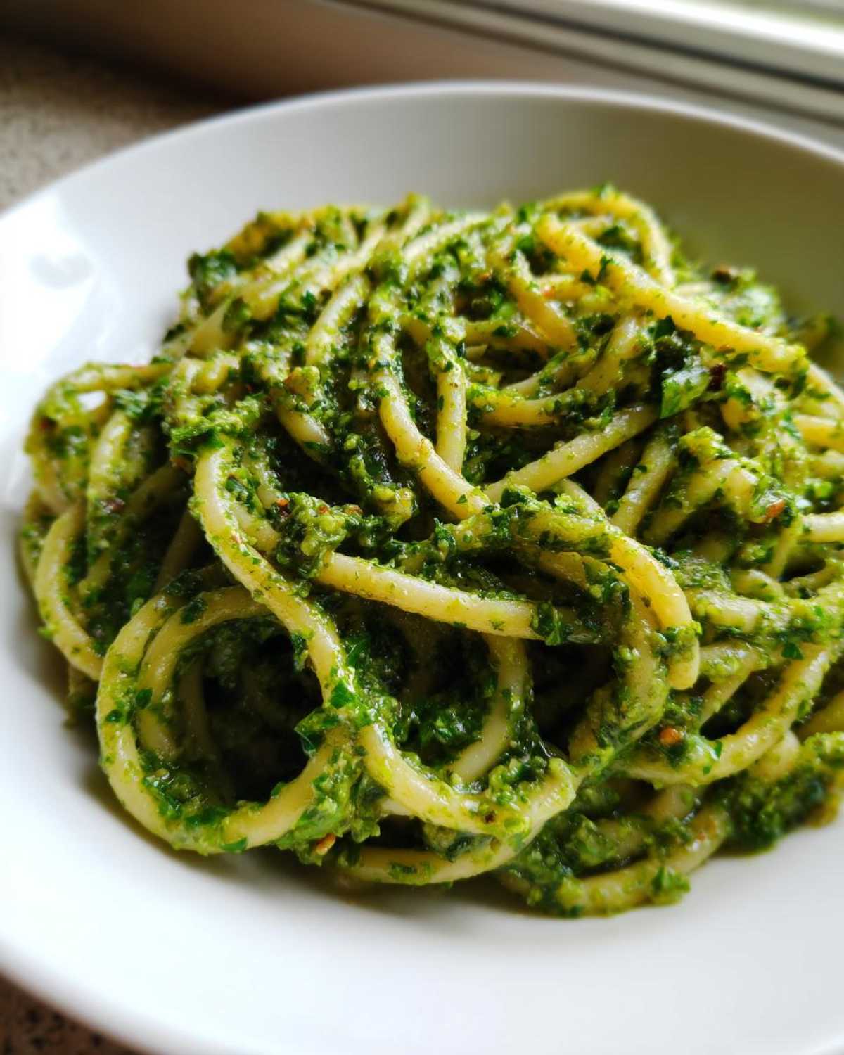 Close-up of thick pasta coated generously with bright green Vegan Basil Pesto in a white bowl.