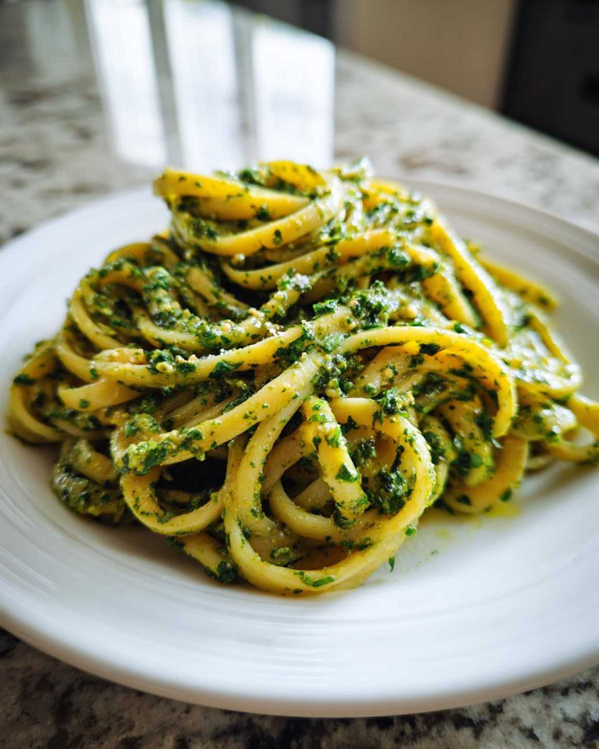 Close-up of pasta generously coated in bright green Vegan Basil Pesto, served on a white plate.