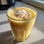 Close-up of a bright yellow Pineapple Coconut Smoothie topped with shredded coconut flakes.