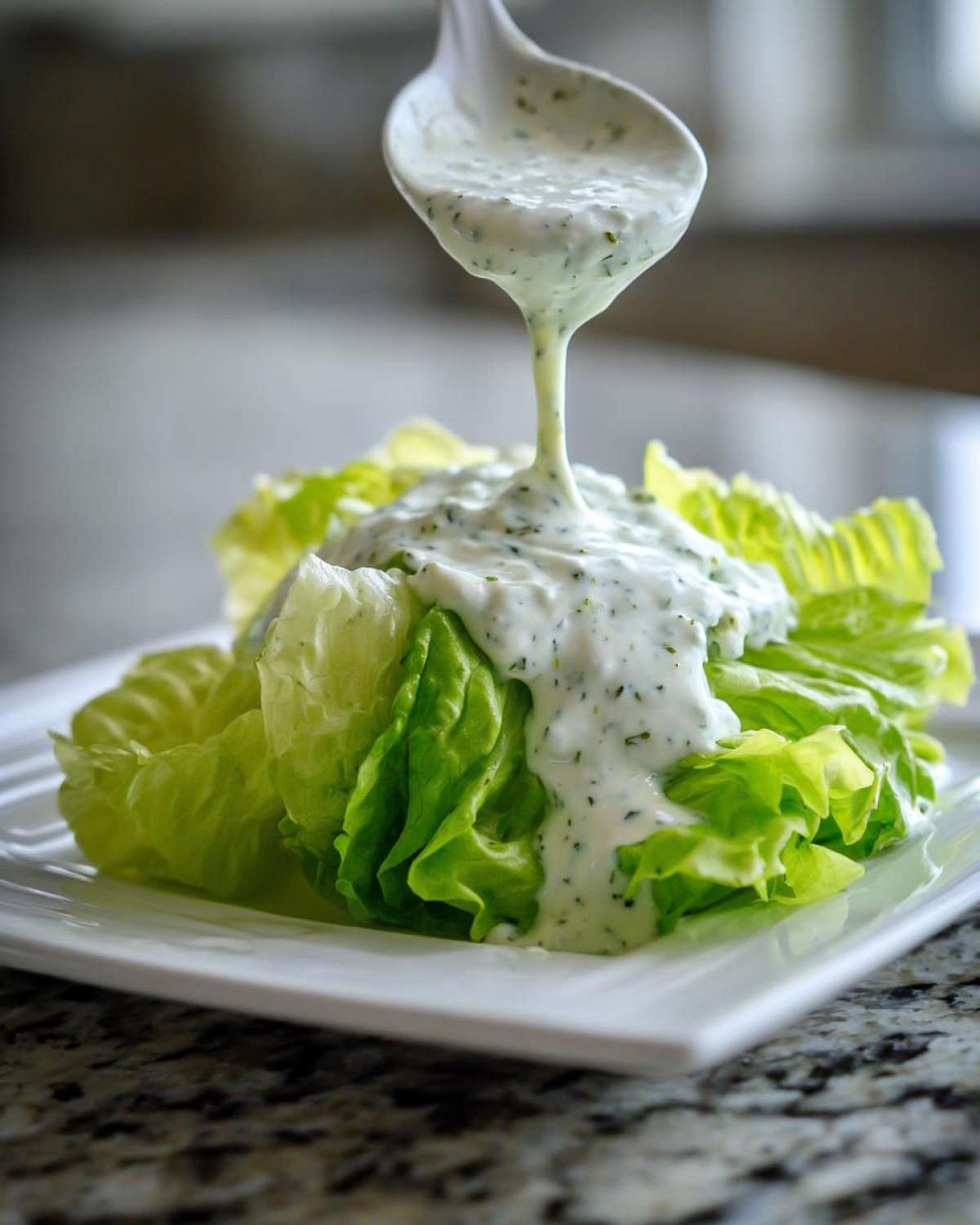 A white spoon pours thick Copycat Olive Garden Salad Dressing over fresh romaine lettuce wedges.
