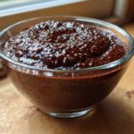 Close-up of rich Vegan Chocolate Chia Pudding texture in a clear glass bowl set on a wooden surface.