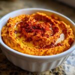 Close-up of creamy Roasted Red Pepper Hummus topped with olive oil and paprika in a white bowl.