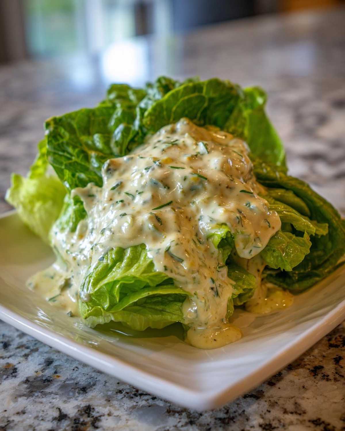 A head of crisp romaine lettuce generously covered in creamy Copycat Olive Garden Salad Dressing on a white plate.