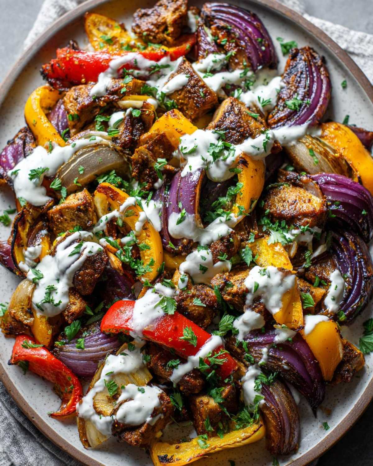Close-up of Sheet Pan Chicken Shawarma with roasted peppers, red onion, and garlic yogurt sauce.