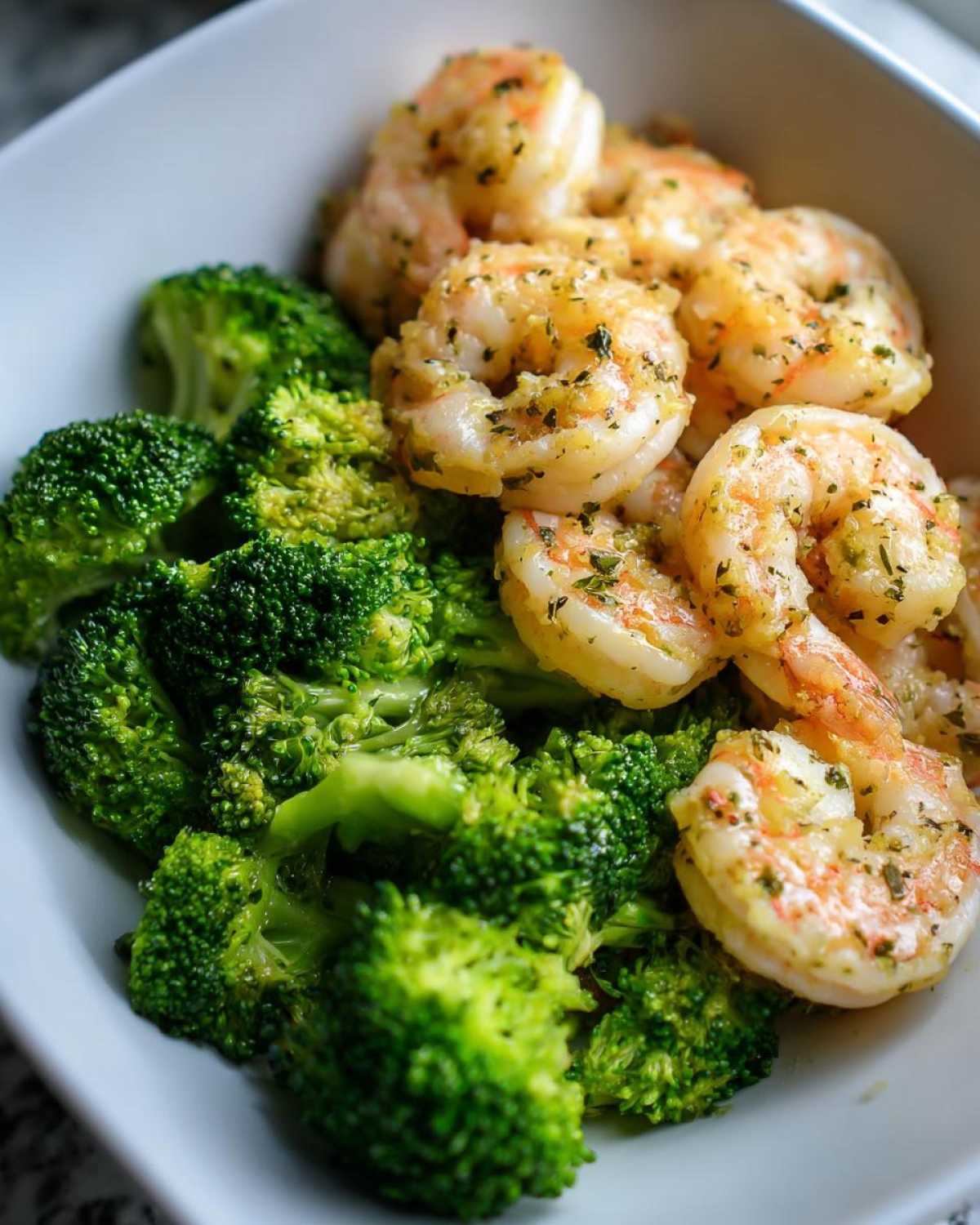 Close-up of cooked shrimp coated in garlic butter and herbs next to bright green broccoli florets.