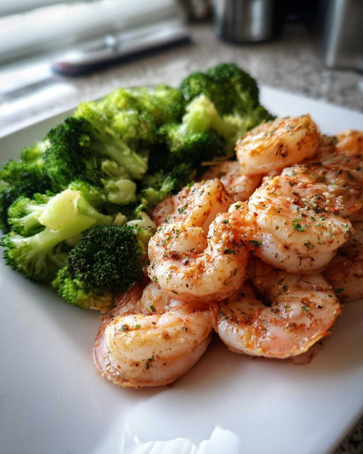 A close-up of cooked shrimp seasoned with herbs next to bright green steamed broccoli, representing Sheet Pan Garlic Butter Shrimp and Broccoli.
