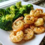 A close-up of cooked shrimp seasoned with herbs next to bright green steamed broccoli florets, showcasing the Sheet Pan Garlic Butter Shrimp and Broccoli.