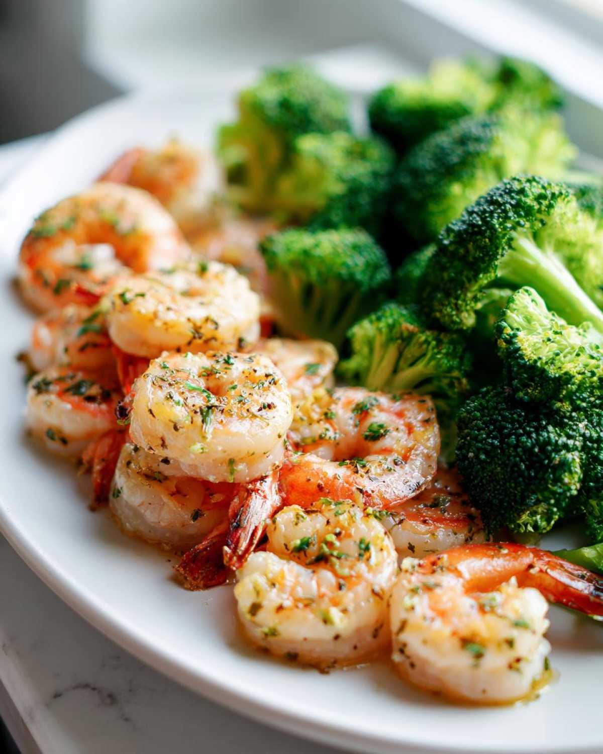 Close-up of cooked shrimp seasoned with garlic and herbs next to bright green broccoli florets from Sheet Pan Garlic Butter Shrimp and Broccoli.