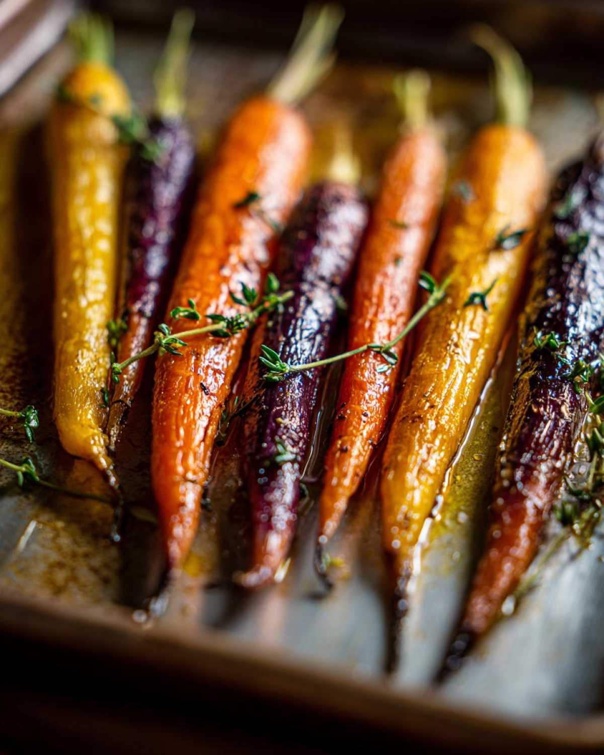 Close-up of glazed Sheet Pan Roasted Rainbow Carrots with Honey and fresh thyme sprigs on a baking sheet.