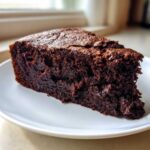 A moist, dark slice of Gluten-Free Chocolate Cake served on a white plate.